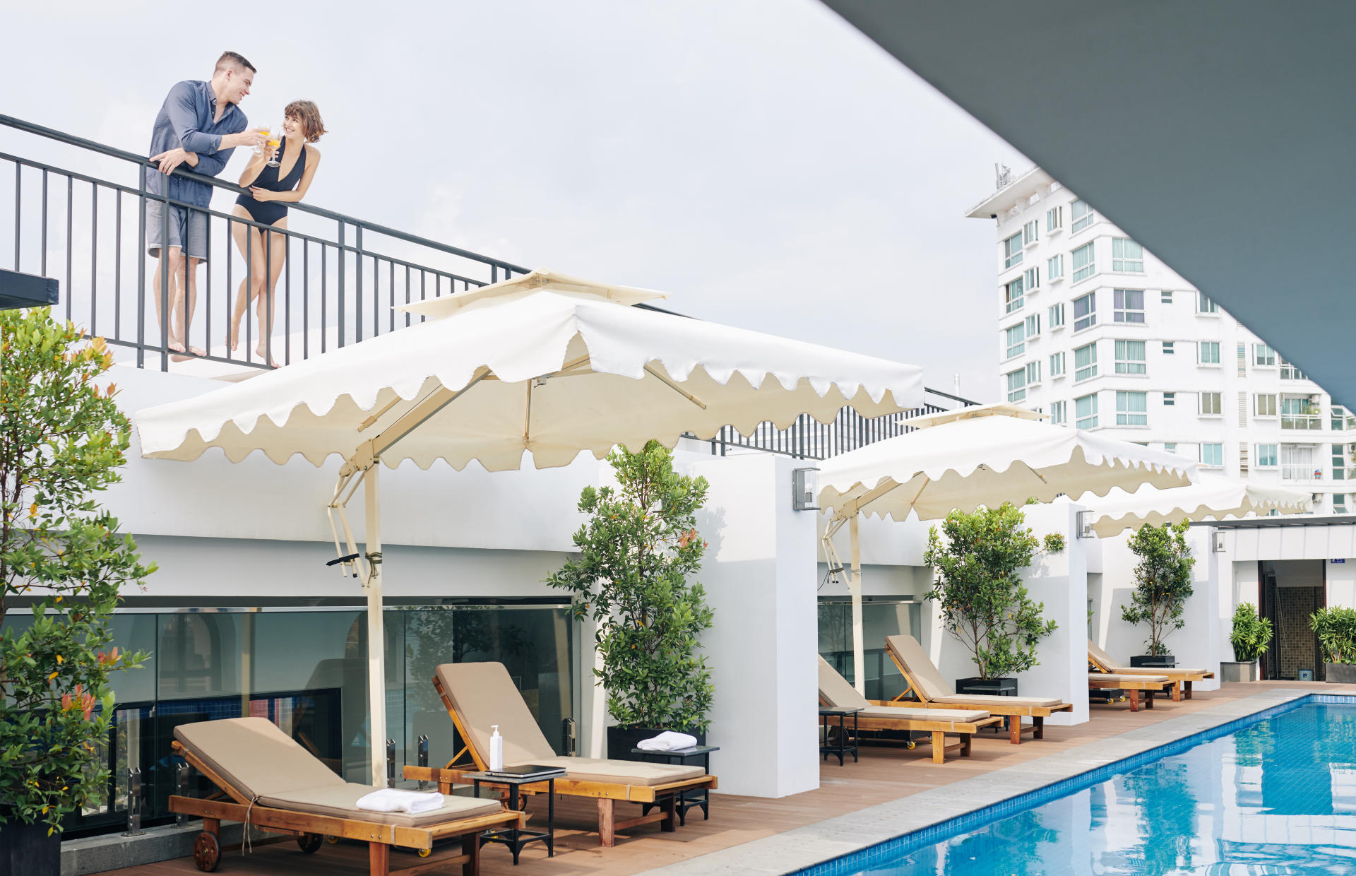 Two hotel guests stand on a balcony above a pool.