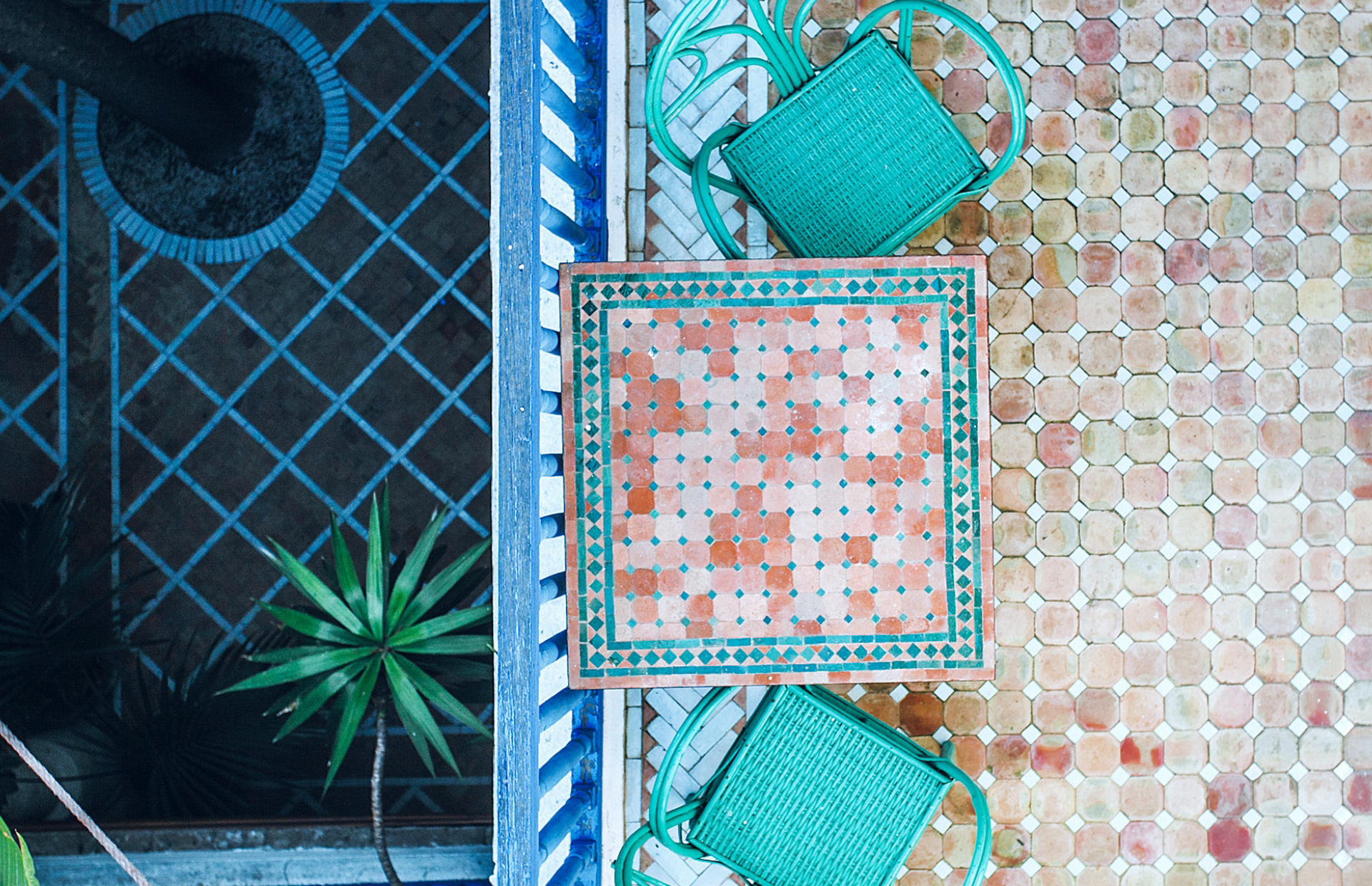 A hotel balcony is furnished with teal chairs and blue and brown tile.