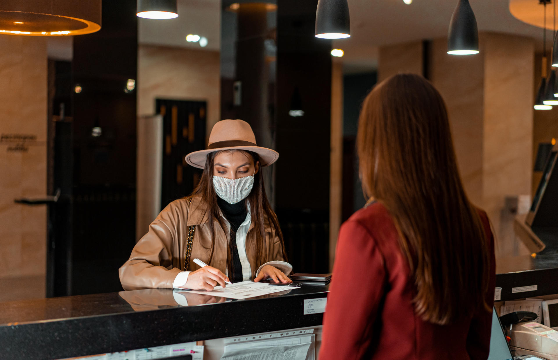 A guest wearing a mask checks in at the front desk.