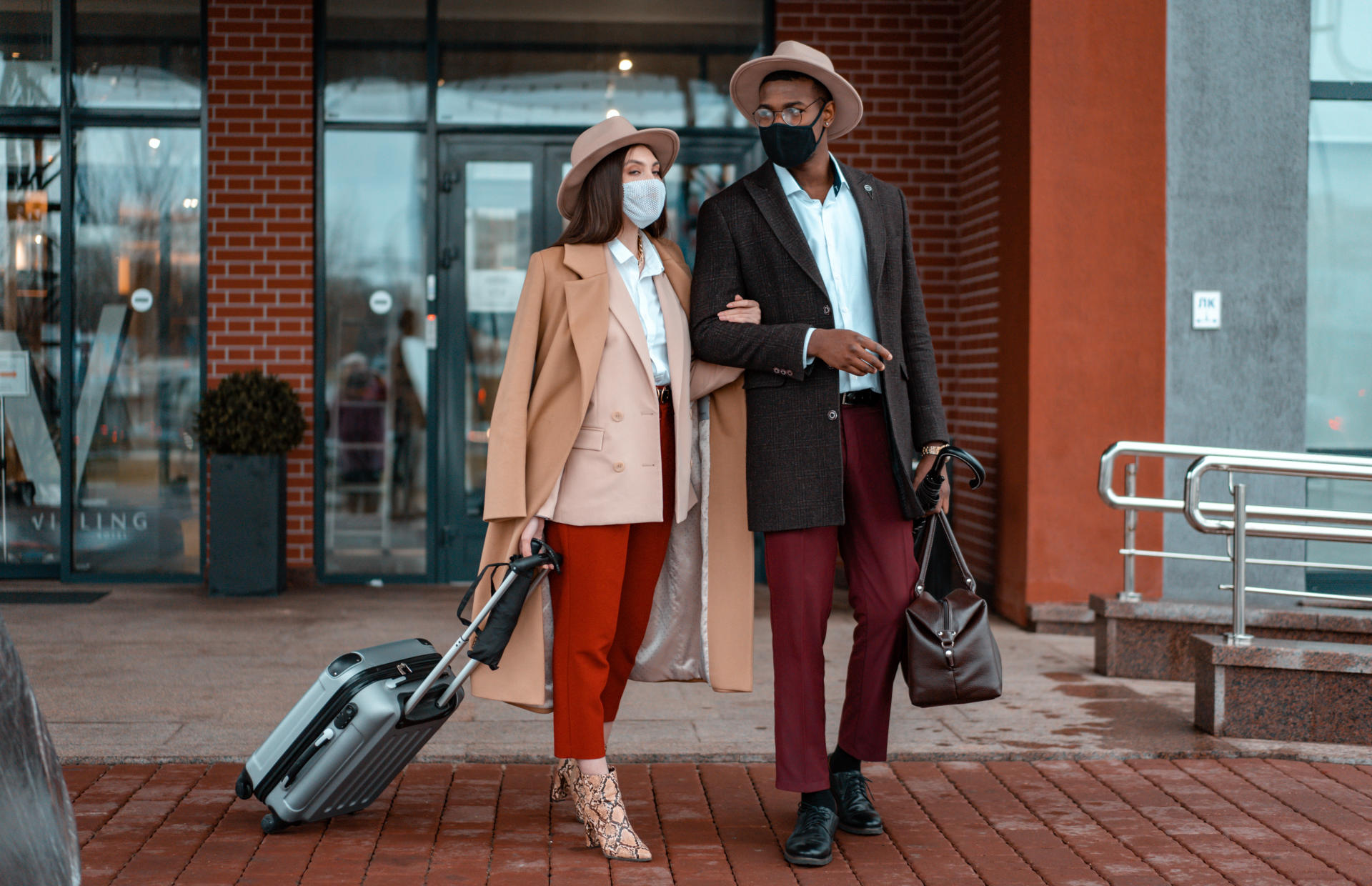 Two hotel guests with masks carry luggage.