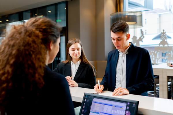 Female hotel receptionist checks in male and female guests.